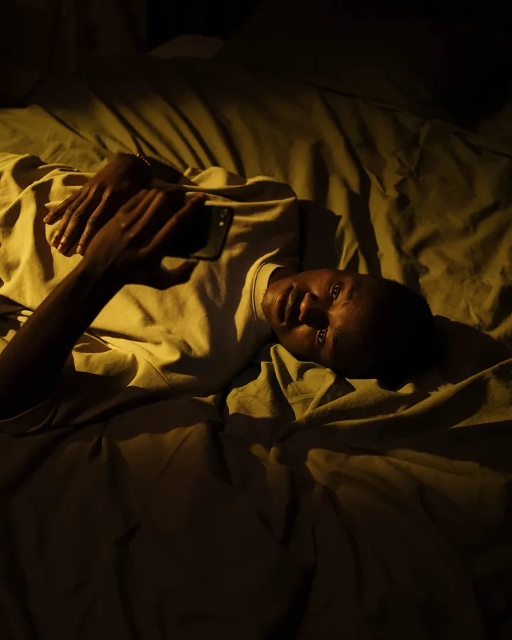 Mann liegt nachts im dunklen Schlafzimmer im Bett und schaut auf sein Handy